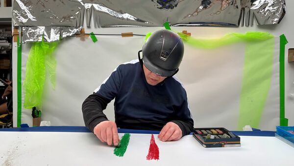 A man in a helmet draws with coloured chalks