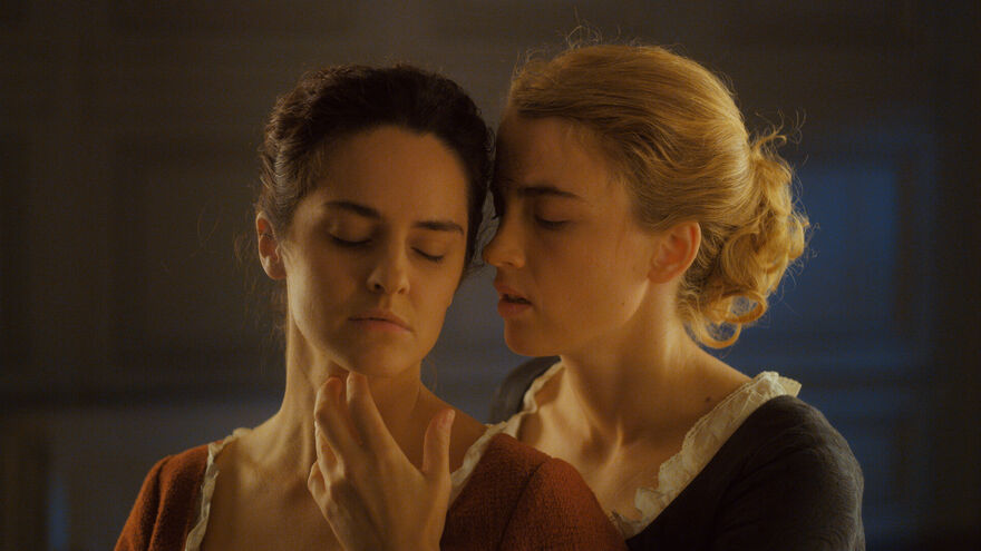 Two women stand closely together, one caresses the other's face. 