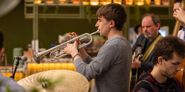 A man in a grey jumper playing the trumpet