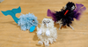 Three craft creature characters made from colourful yarn pompoms, card, and feathers.