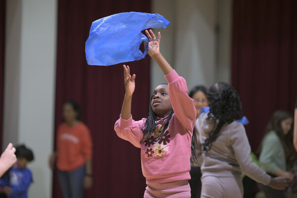 Young girl participating in movement workshop, arms in the air with a blue plastic bag