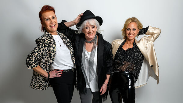 3 women smiling at camera, one with a hand on her hip and two with one hand on their head