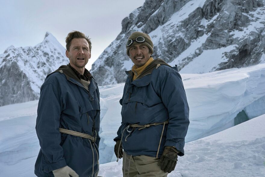 Tom Hiddleston as Edmund Hillary and Genden Phuntsok as Tenzing Norgay standing on a snowy mountainside. 