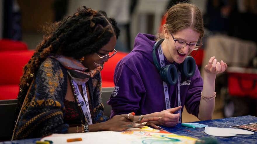 Two university students smiling and collaborating on a creative activity.