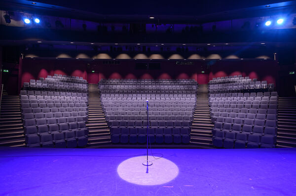 A microphone stand in a spotlight on stage, looking out to an empty auditorium