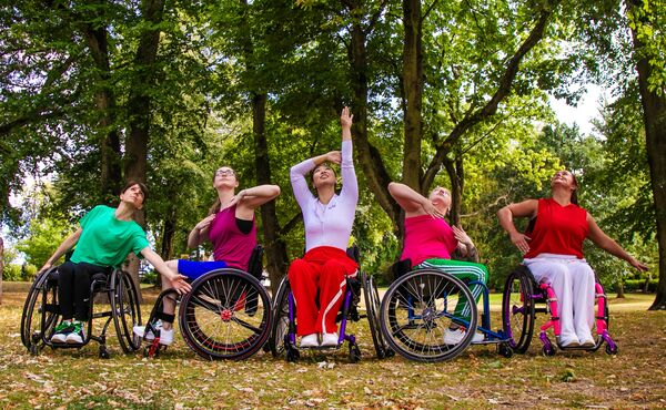 5 people in wheelchairs with green trees behind them