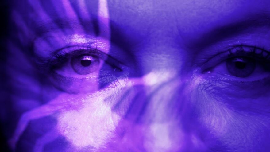 An extreme close-up of a woman's eyes bathed in violet light. 