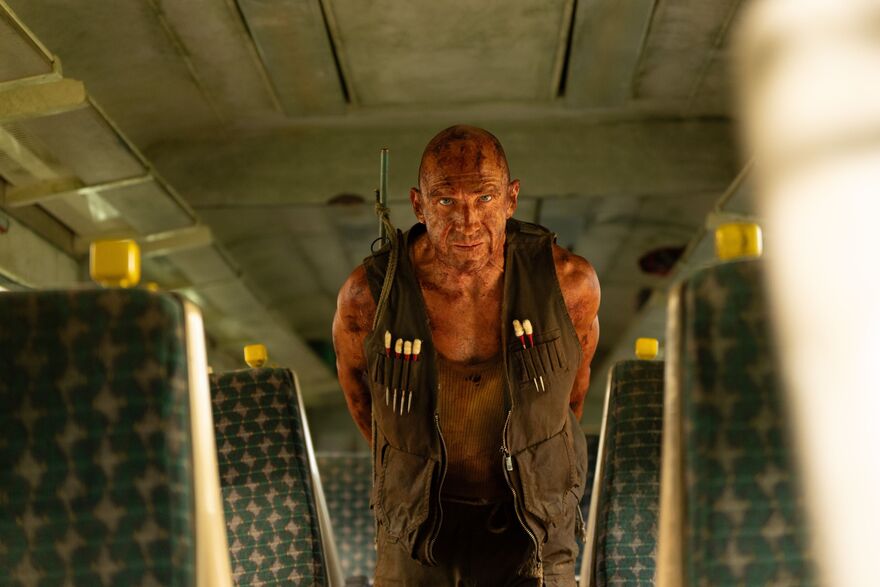 A man covered in dried blood walks through an empty bus. 