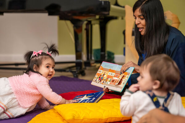 Two young children on the floor with a woman showing them a book