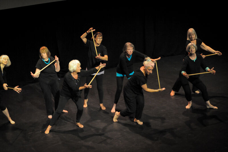 Elders dance performers in black performing holding long batons