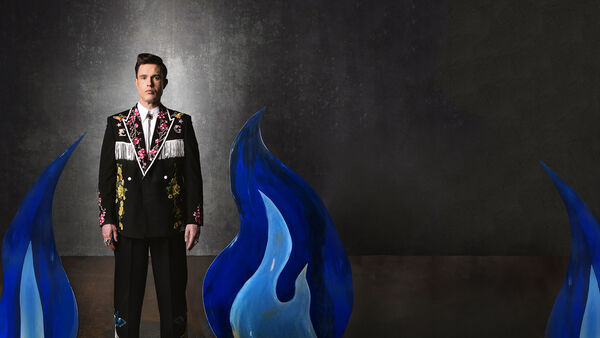 Ed gamble in a black sit with flowery lapels with blue flames on either side of him