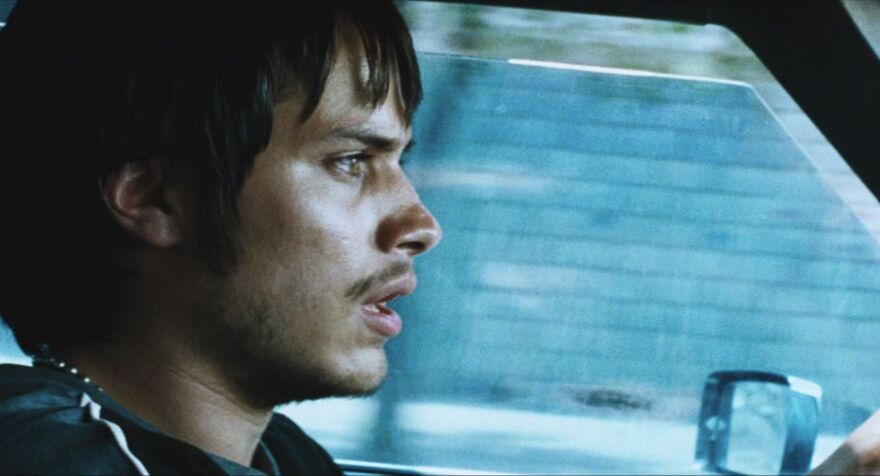 A young man drives a car looking concerned. 