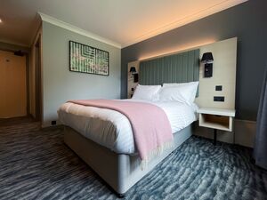A doule bed hotel bedroom with a grey, pink, green and white colour pallet.