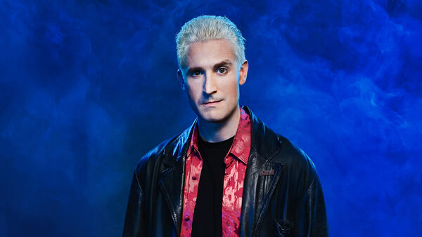 Comedian Brendan Murphy in character as Spike from Buffy the Vampire Slayer, wearing a black leather jacket against a smoky blue background.