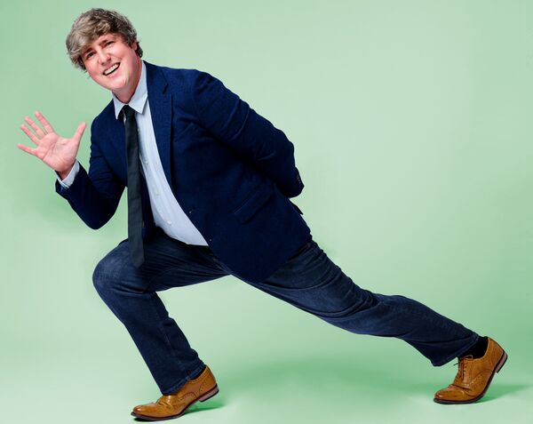 Glenn Moore in a suit leaning and waving with a mint green backgorund
