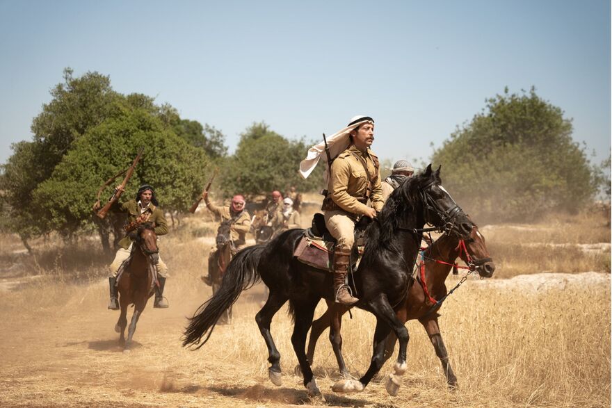 Men ride on horseback along a dusty road. 