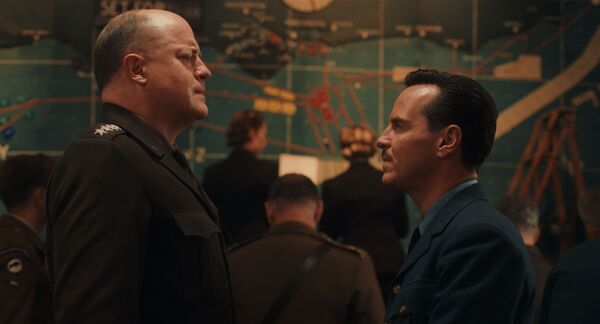 Two men in military uniform stand opposite one another. One is much taller than the other. A military map can be seen in the background. 