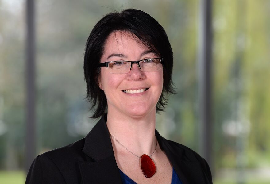 Headshot of Andrea Pulford with red necklace against backdrop of windows and green space.  