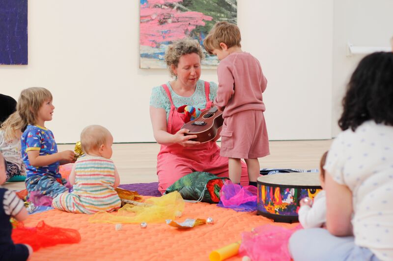 Child standing up looking at adult holding a banjo