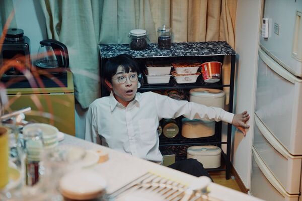 A shocked man cowers on a kitchen floor. 