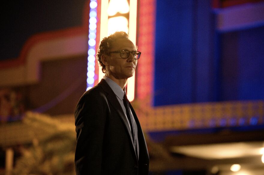 A well dressed man stands in front of glittering lights. 