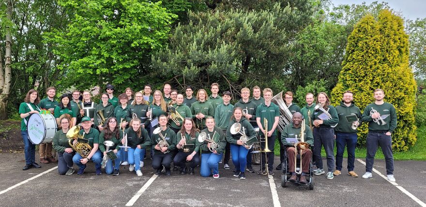 Brass Society all wearing green standing in front of trees