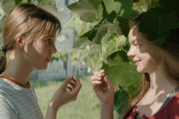 Two teenage girls stand opposite each other amongst greenery. 