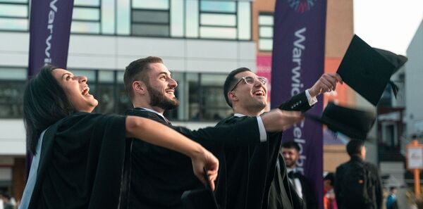 3 students in graduation gowns throwing their hats in the air