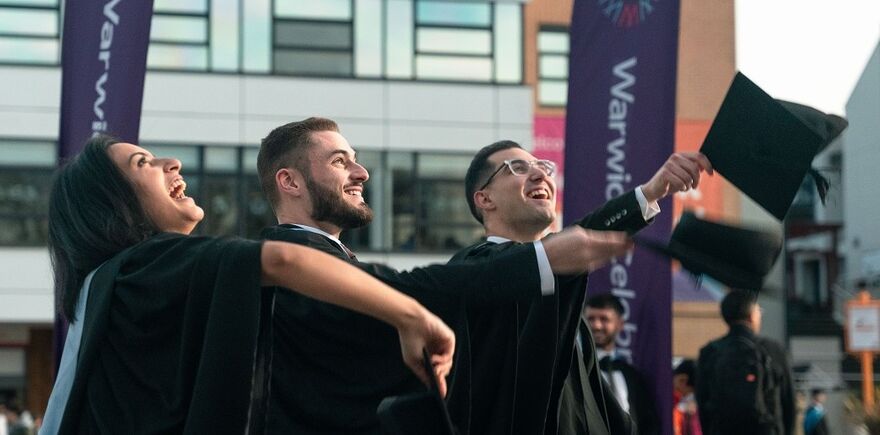 3 students in graduation gowns throwing their hats in the air