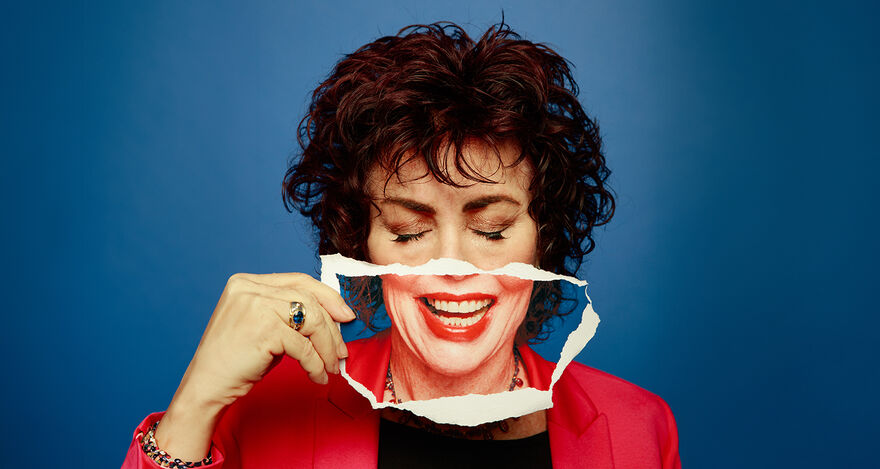Ruby Wax with her eyes closed holding a photo of her smiling over her mouth