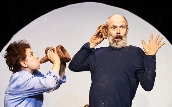 A man holding a clay ear to his face and a woman blowing a clay horn