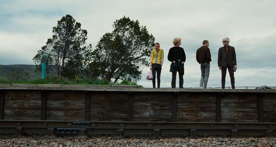Four men stand on the edge of a train platform. 