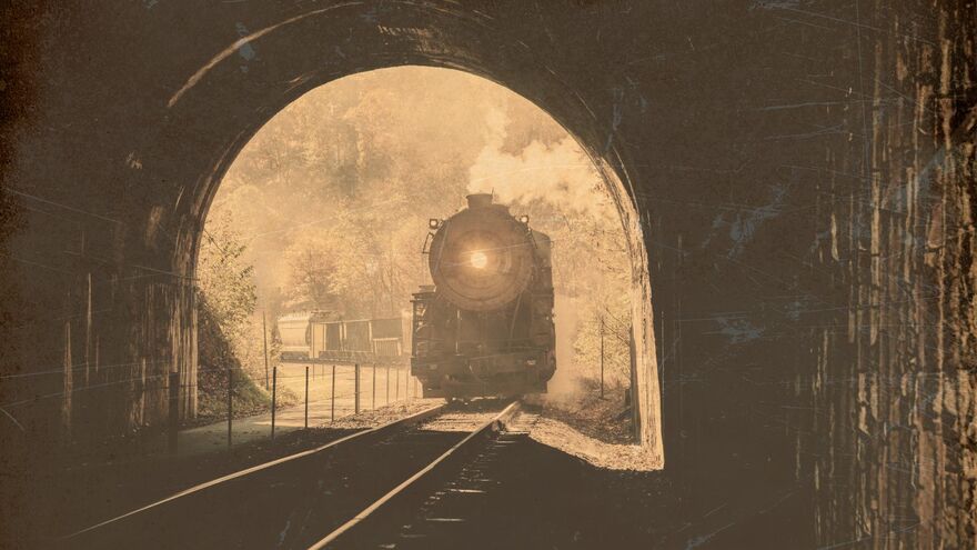 A sepia toned image of a steam train entering a tunnel. 