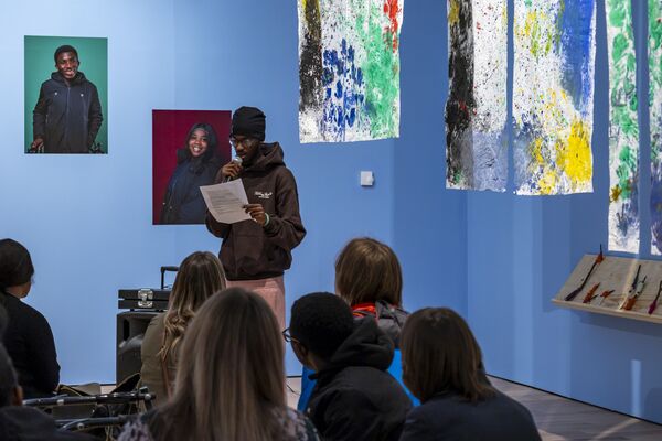 Person stood up reading from a sheet of paper with several people sat watching