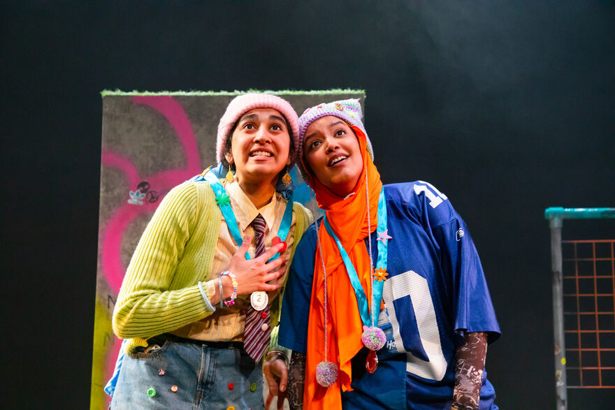 Two hijab-wearing girls stand next to each other, looking into the distance wearing medals