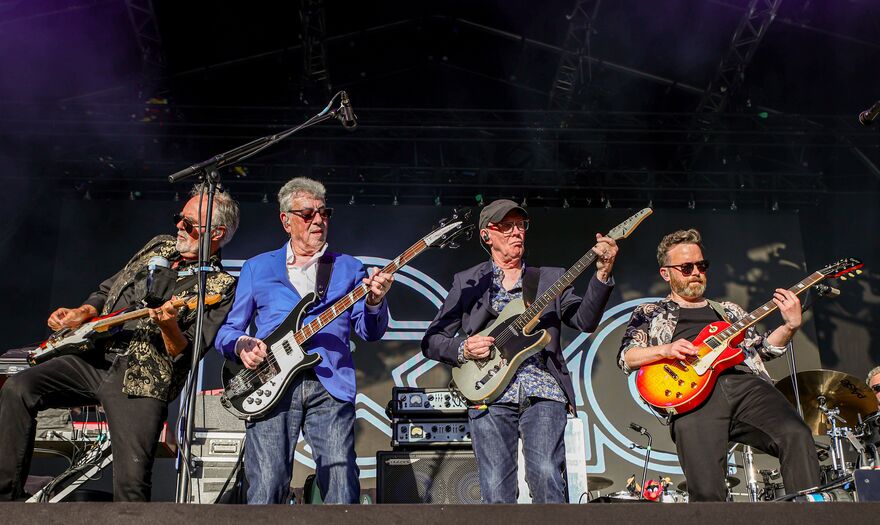 Four men with guitars stand at the front of the stage
