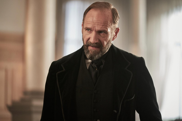 Ralph Fiennes in a black jacket looking of to the left of the screen