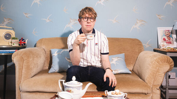 Josh Widdicombe sitting on a cream sofa holding a china tea cup