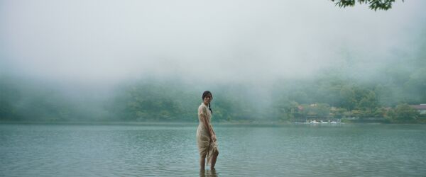 A young woman looks to camera as she paddles in a lake. The background is misty. 