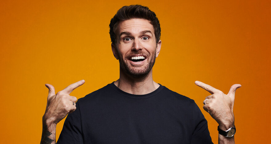Joel Dommett pointing himself against an orange background