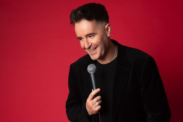 Jarlath Regan holding a microphone and standing in front of red background