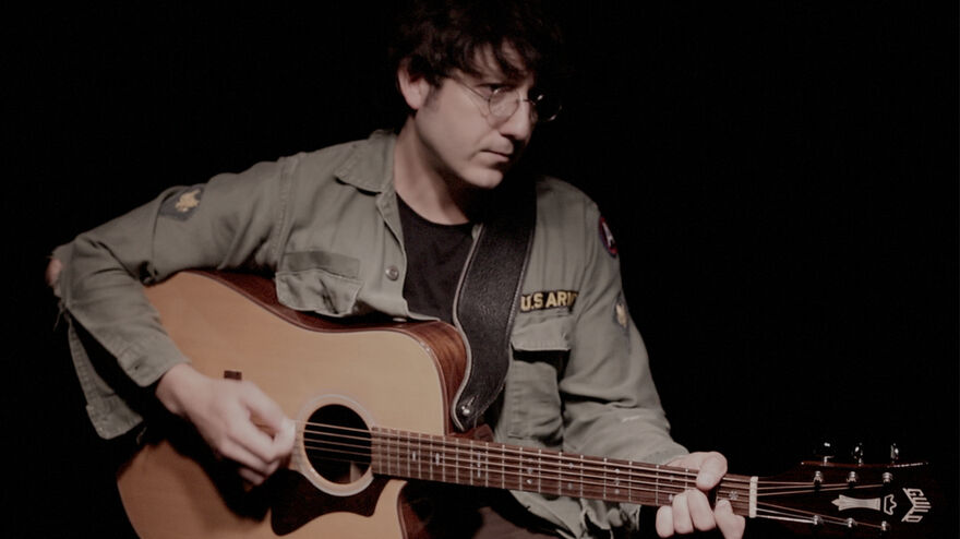 Tyson Kelly as John Lennon playing guitar