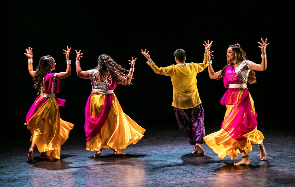 Nupur dancers in vibrant yellow, purple and pink clothes dance on stage