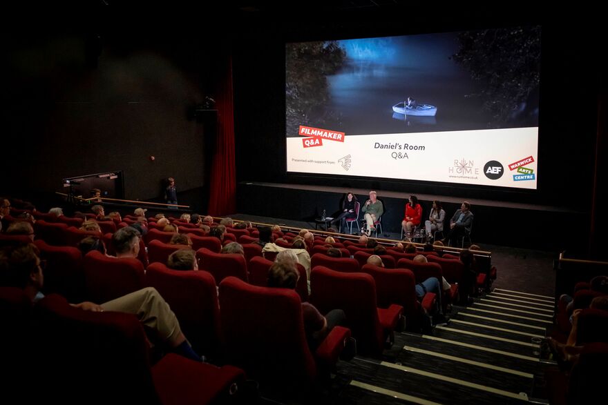 A full cinema screen with speakers hosting a Q+A. 