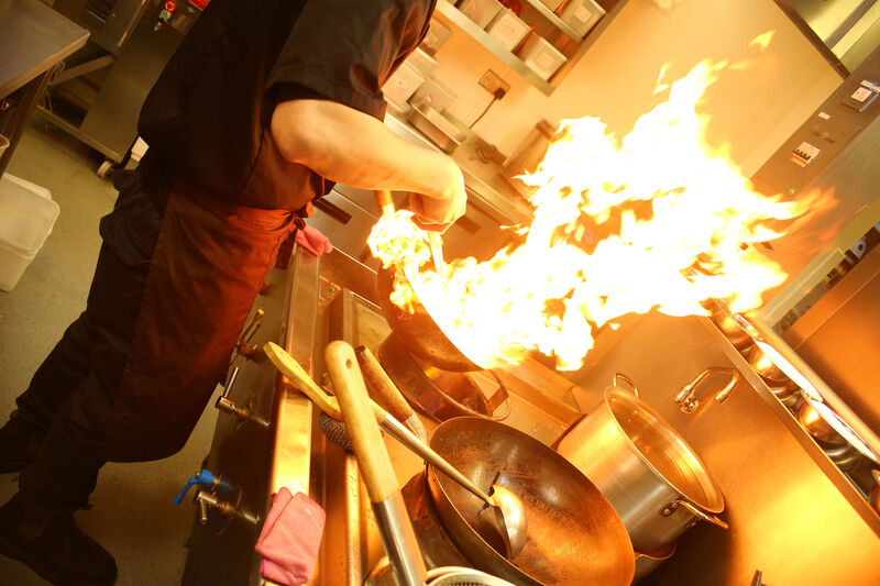 A chef tending to a pan on fire in a kitchn