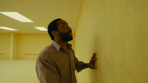 A man with wide eyes stares at a blank beige wall. 