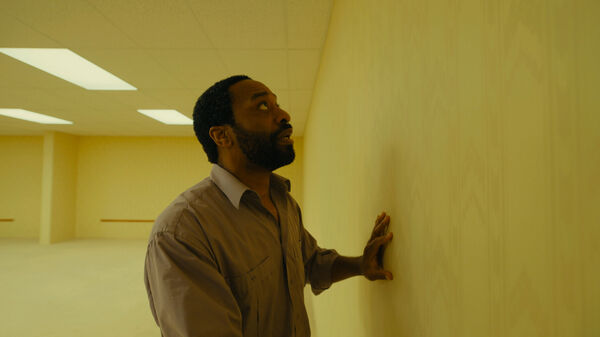 A man with wide eyes stares at a blank beige wall. 