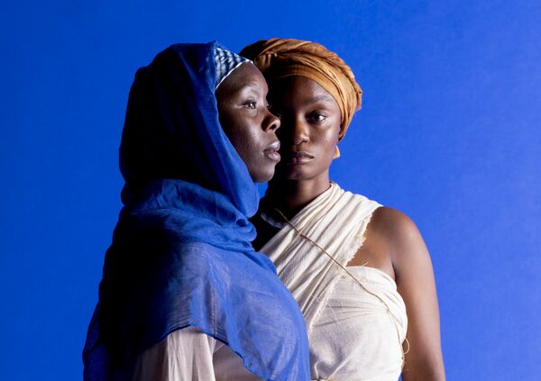 Two women - one looking forward, the other to the side - blue background