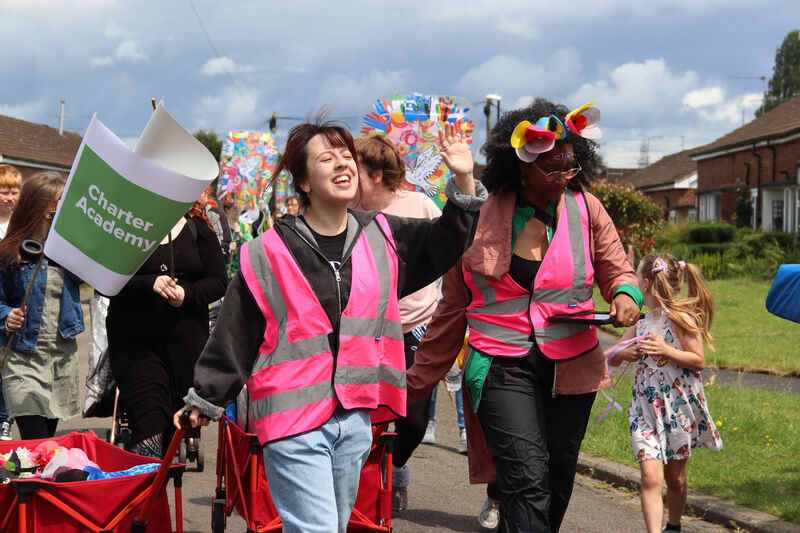 Two women walk in the Canley Parade wearing bright pink safety vests over their clothes.