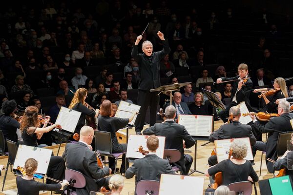 Sir Mark Elder standing and conducting orchestra with audience in the background